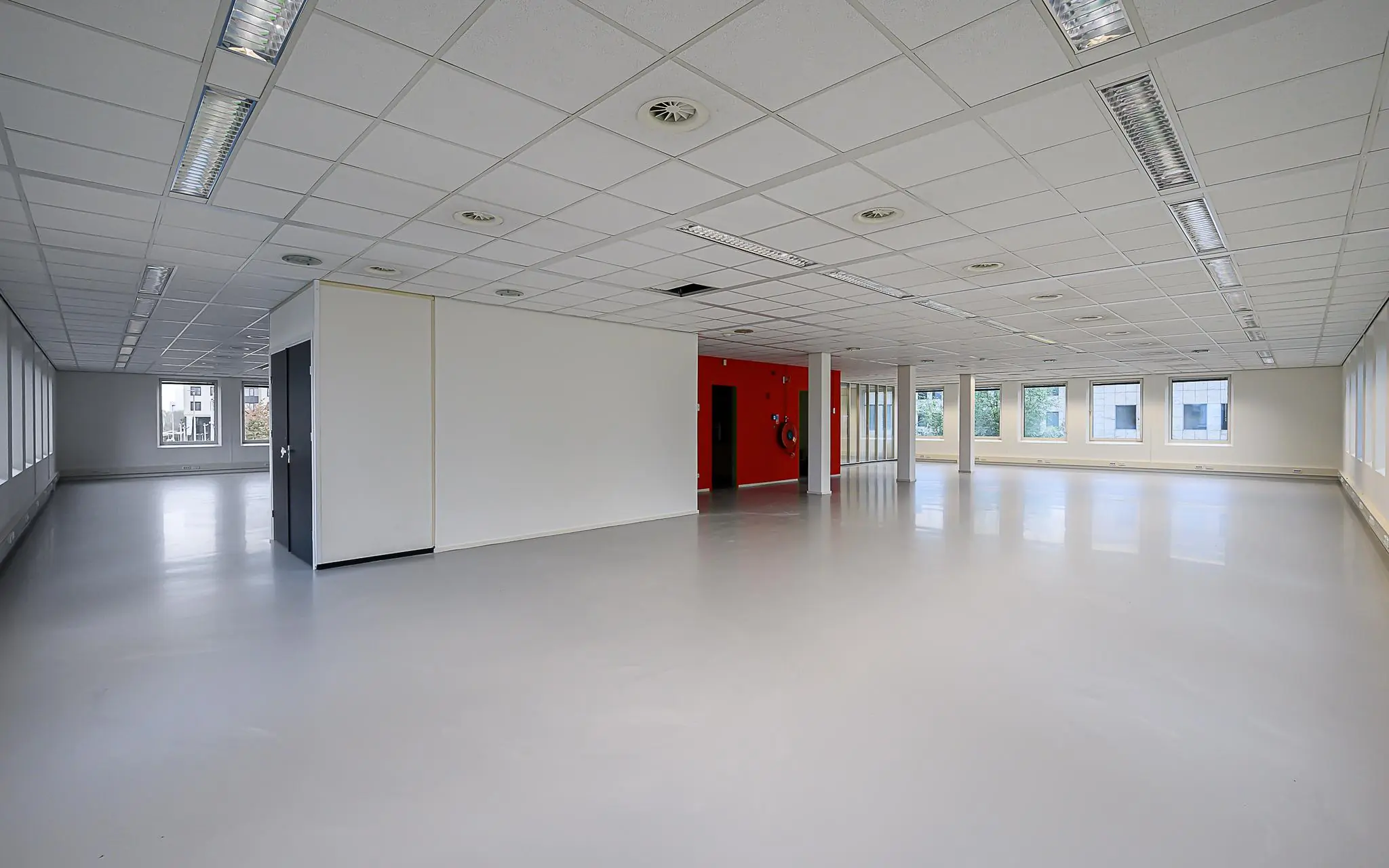 Leeg en modern kantoorruimte-interieur aan de Rivium Westlaan met grote ramen en systeemplafond.